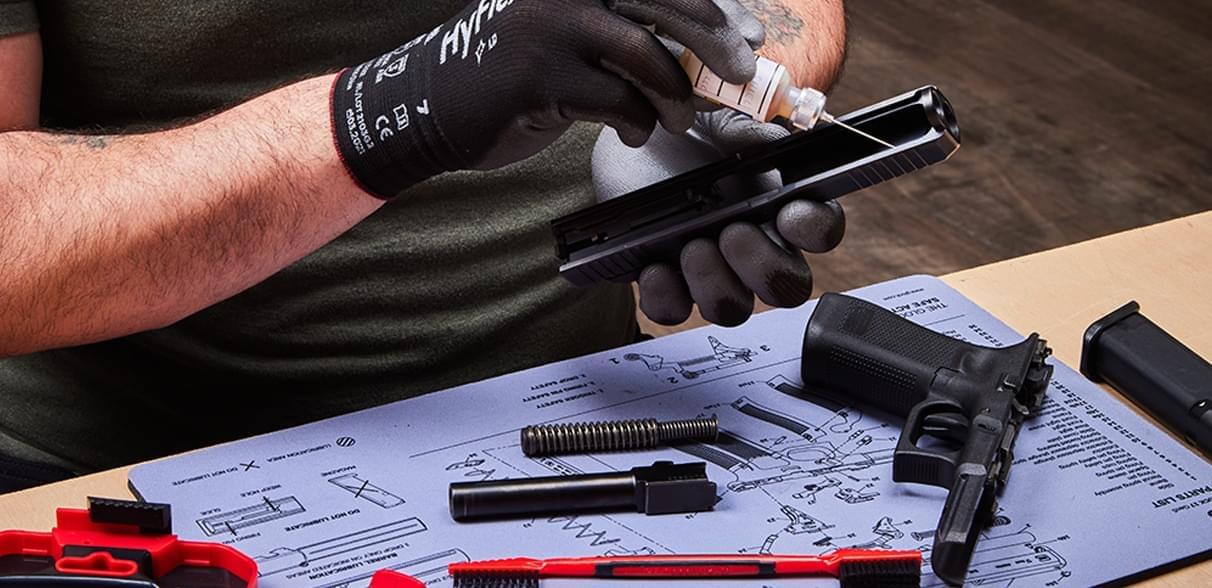 Hands cleaning a handgun and lubricating the slide